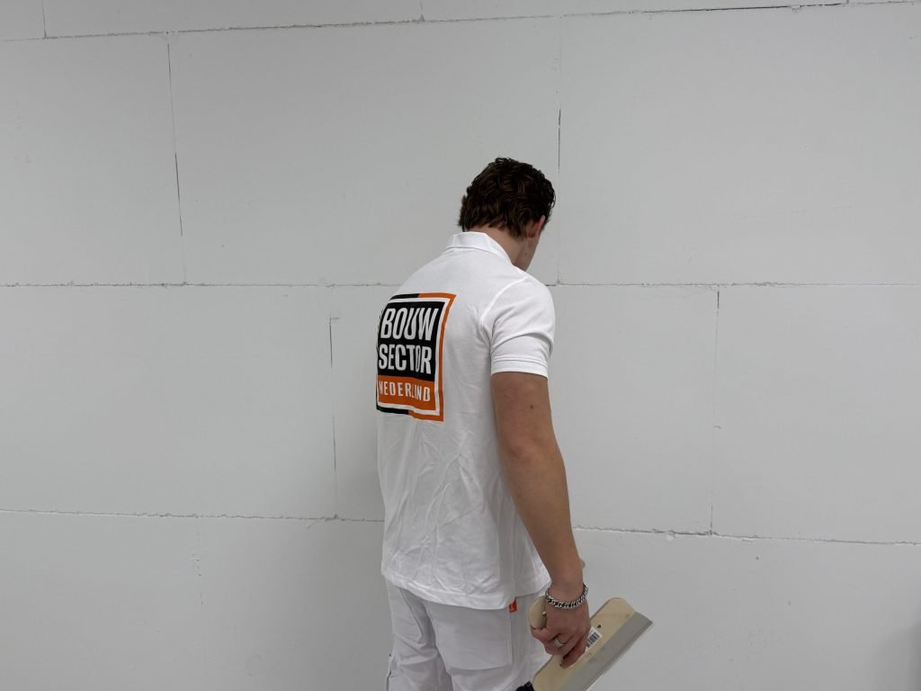 Stukadoor van Bouwsector Nederland staat met een plakspaan voor een kale wand van gipsblokken met zichtbare voegen