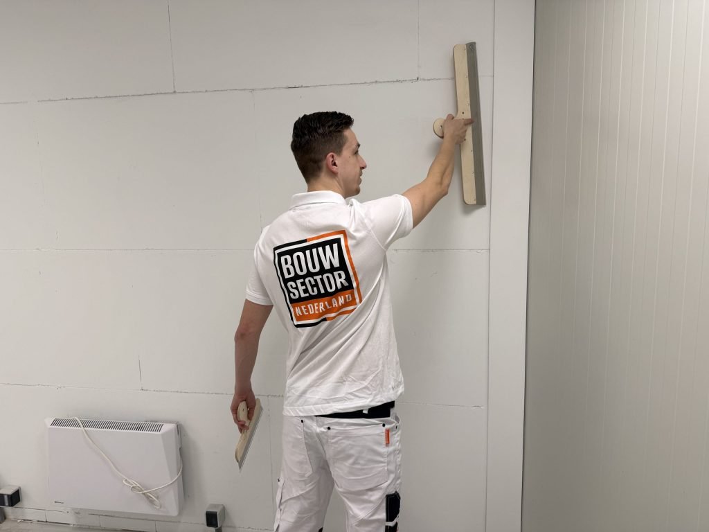 Stukadoor met een spaan in elke hand werkt een wand naast een elektrische kachel af